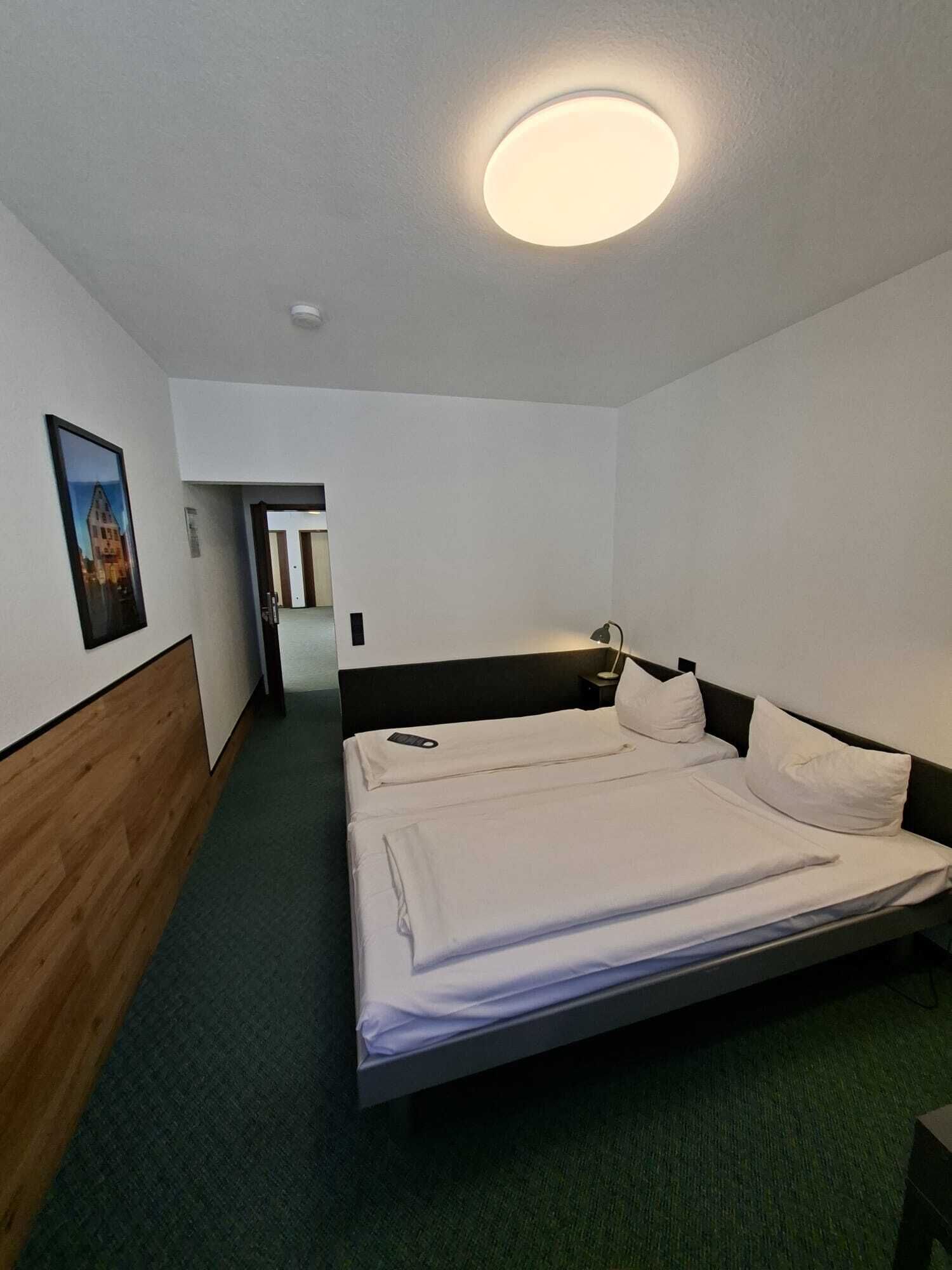 Une chambre d’hôtel avec un lit simple, une table de chevet, une lampe et un tableau encadré au mur.