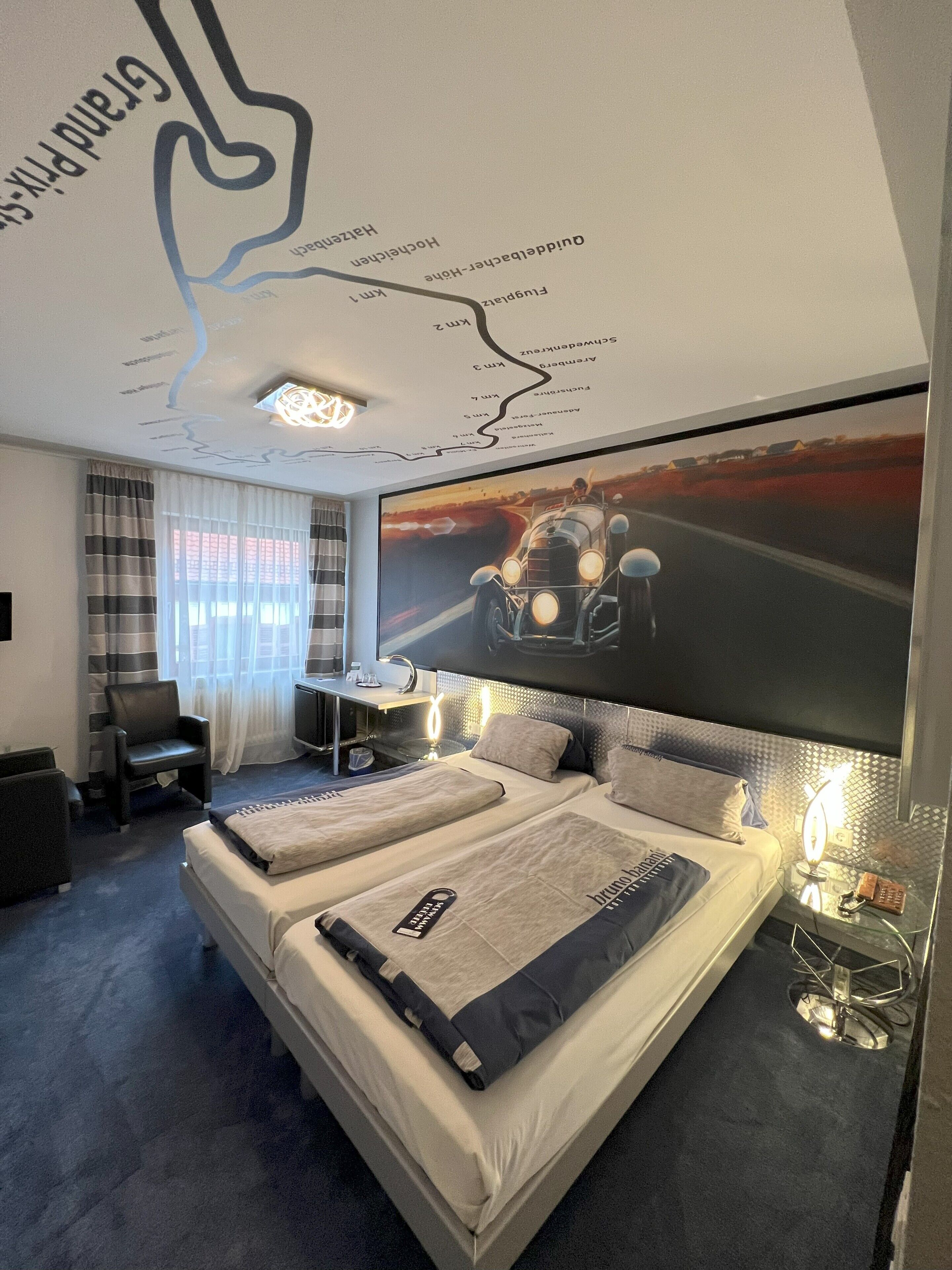 Ein modernes Hotelzimmer mit einem großen Bett, einem Schreibtisch, einem Sessel und einer großen Wandmalerei.