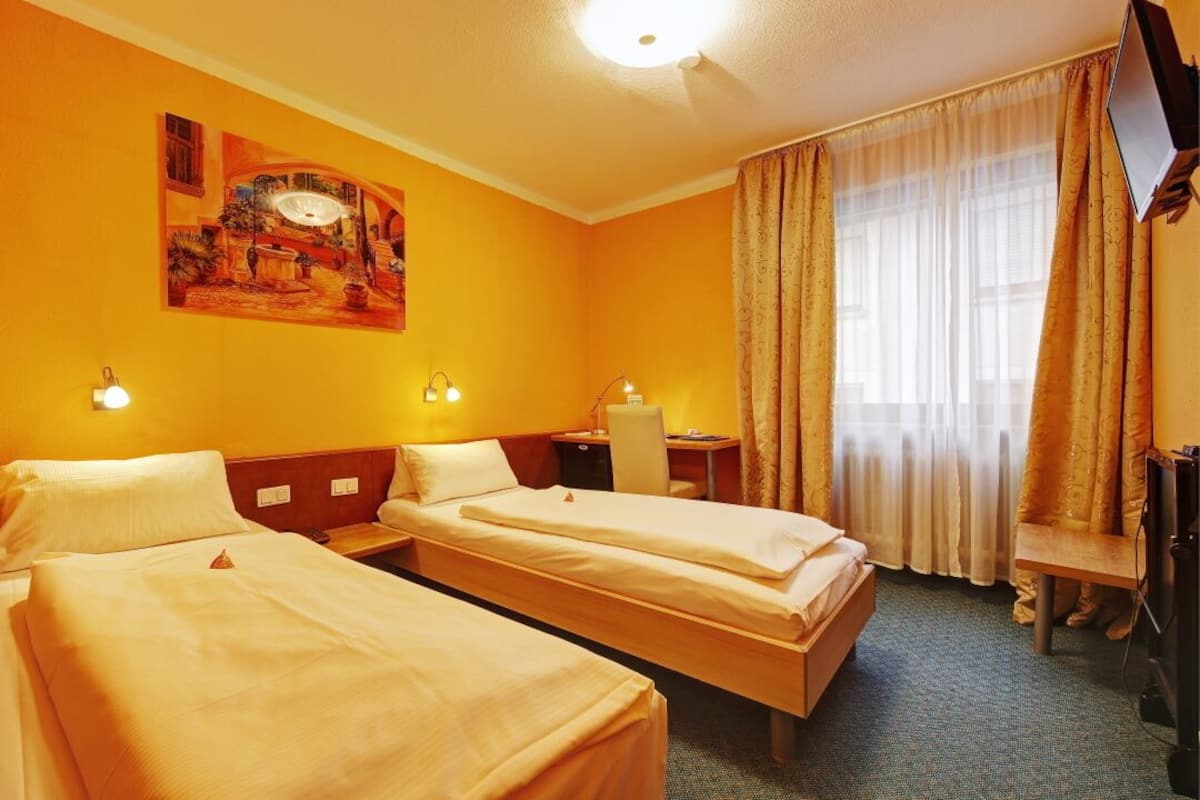 A hotel room with two beds, a painting on the wall, a desk, and a television.