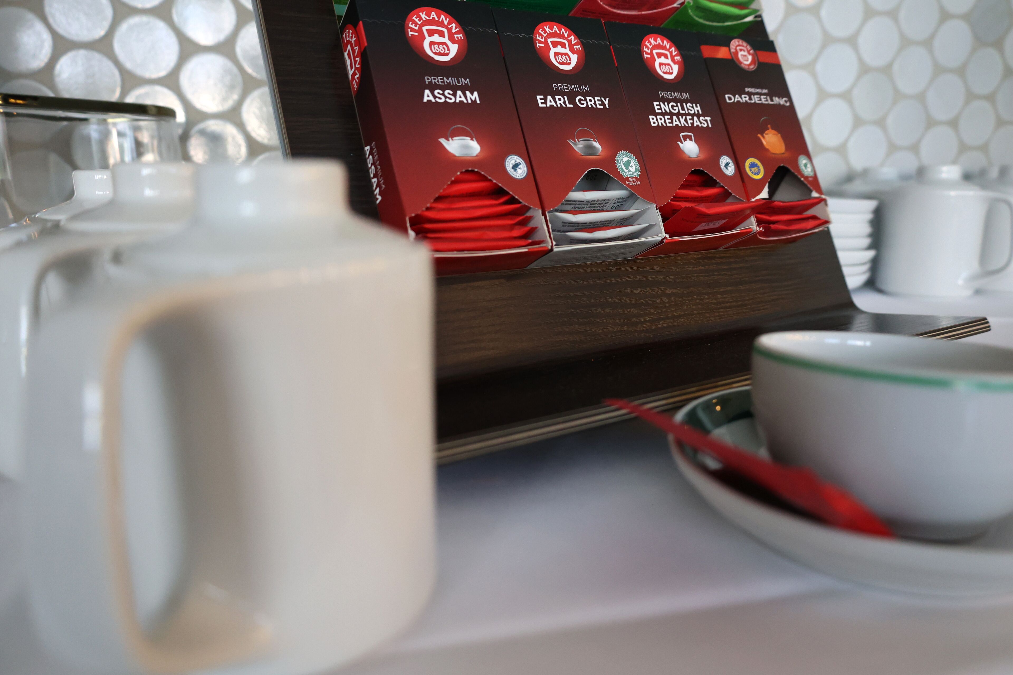 Una escena de desayuno con una tetera, tazas y una caja de variedades de té premium.