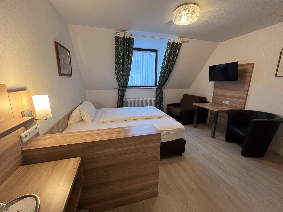 A hotel room with a bed, a desk, a chair, a TV, and a window with curtains.