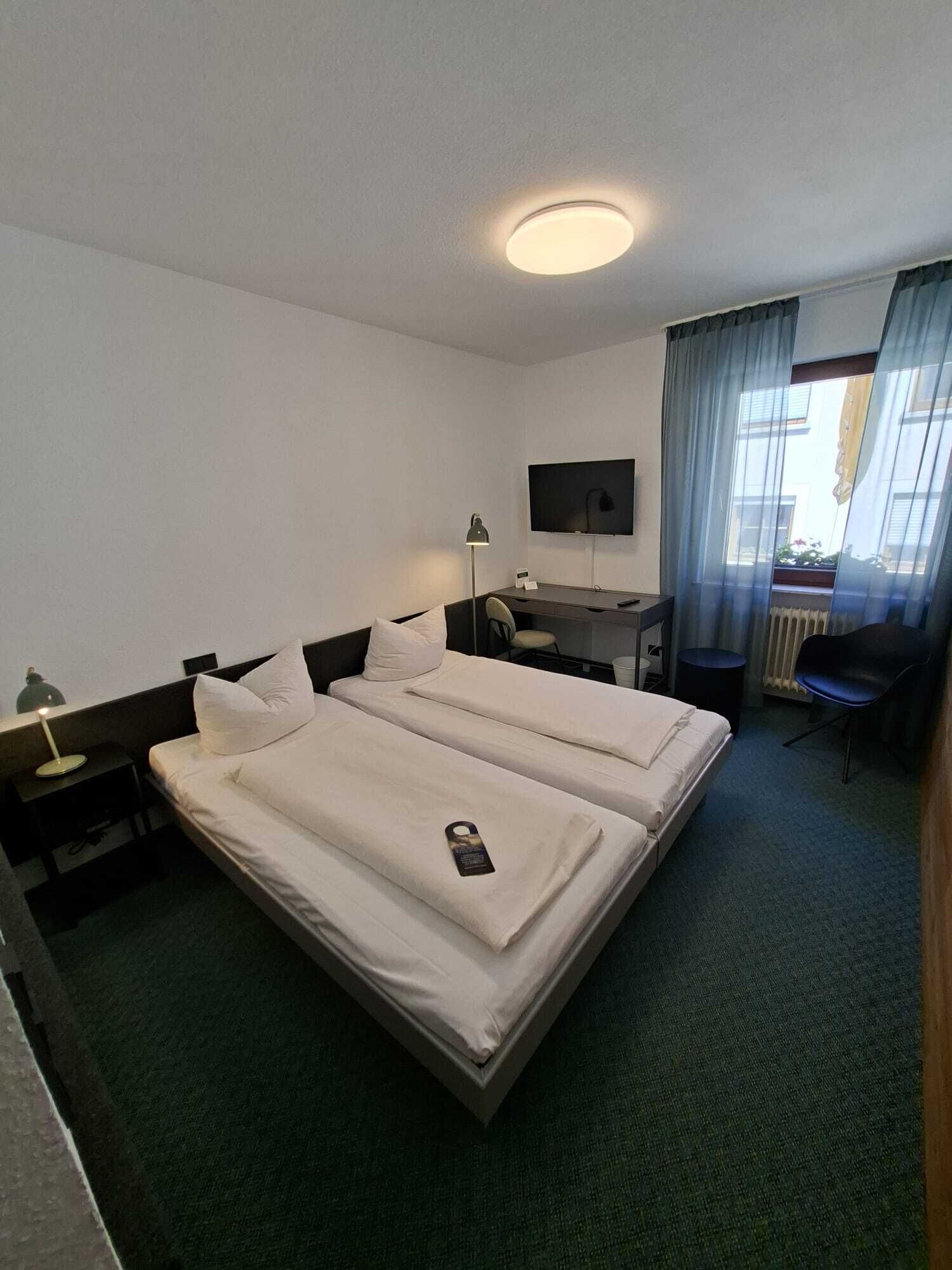 A hotel room with a bed, desk, chair, TV, and a window with curtains.
