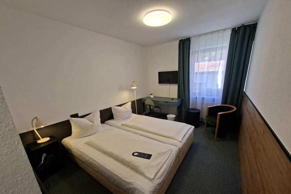 A hotel room with two beds, a desk, a chair, a TV, and a window with curtains.