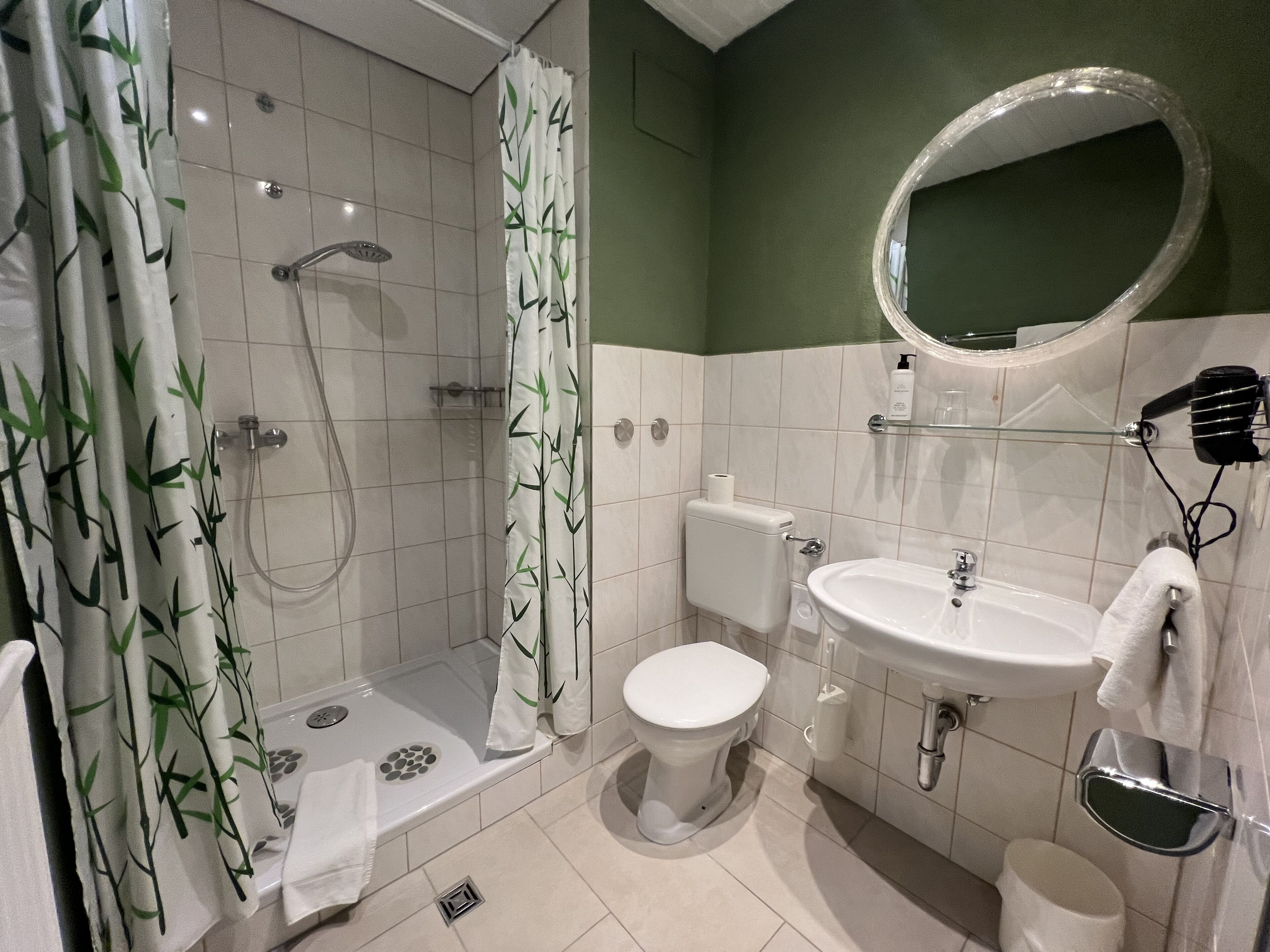 A bathroom with a shower, toilet, sink, and a mirror.