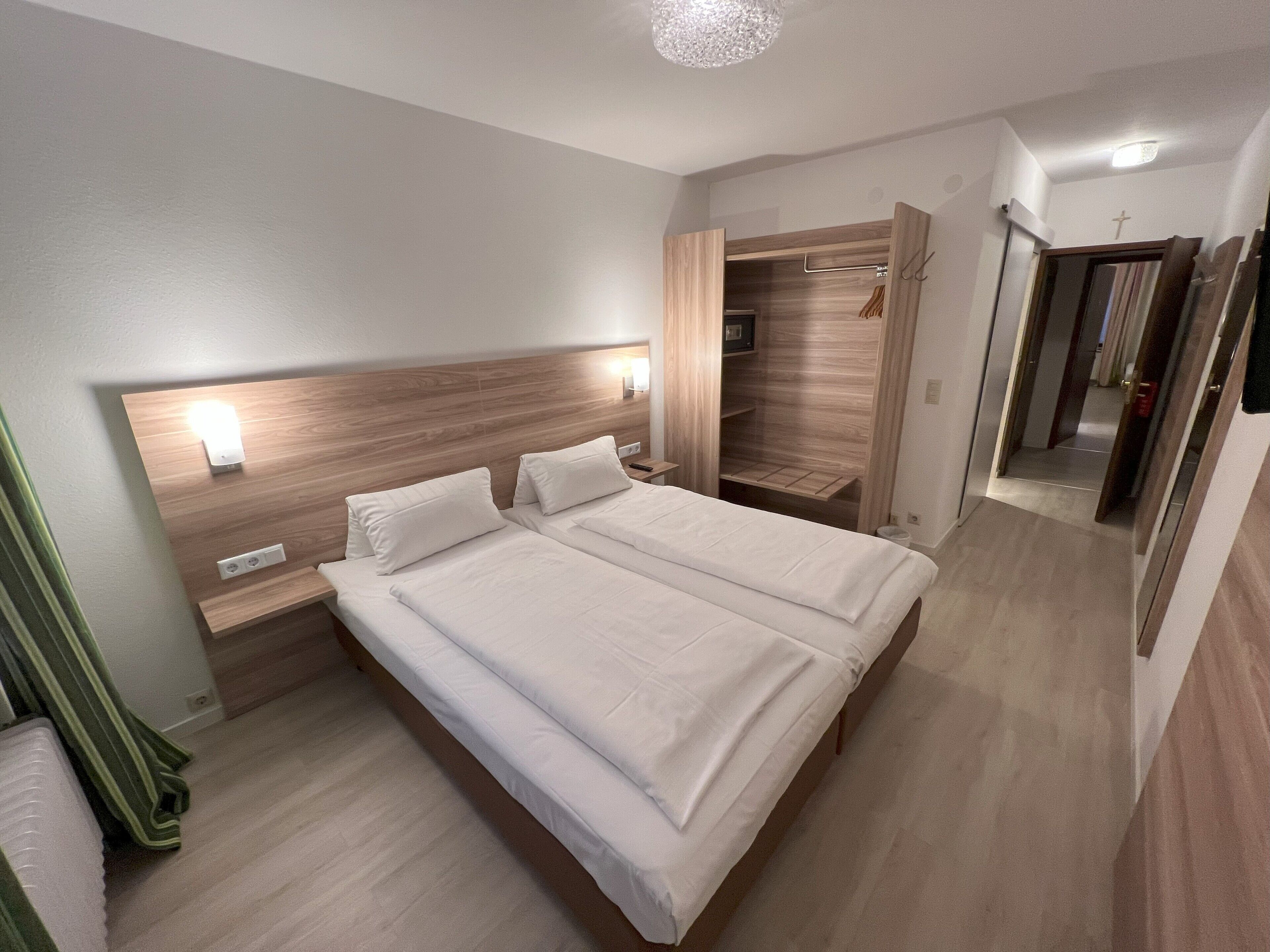 A modern hotel room with a large bed, bedside tables, a built-in wardrobe, and a mirror.