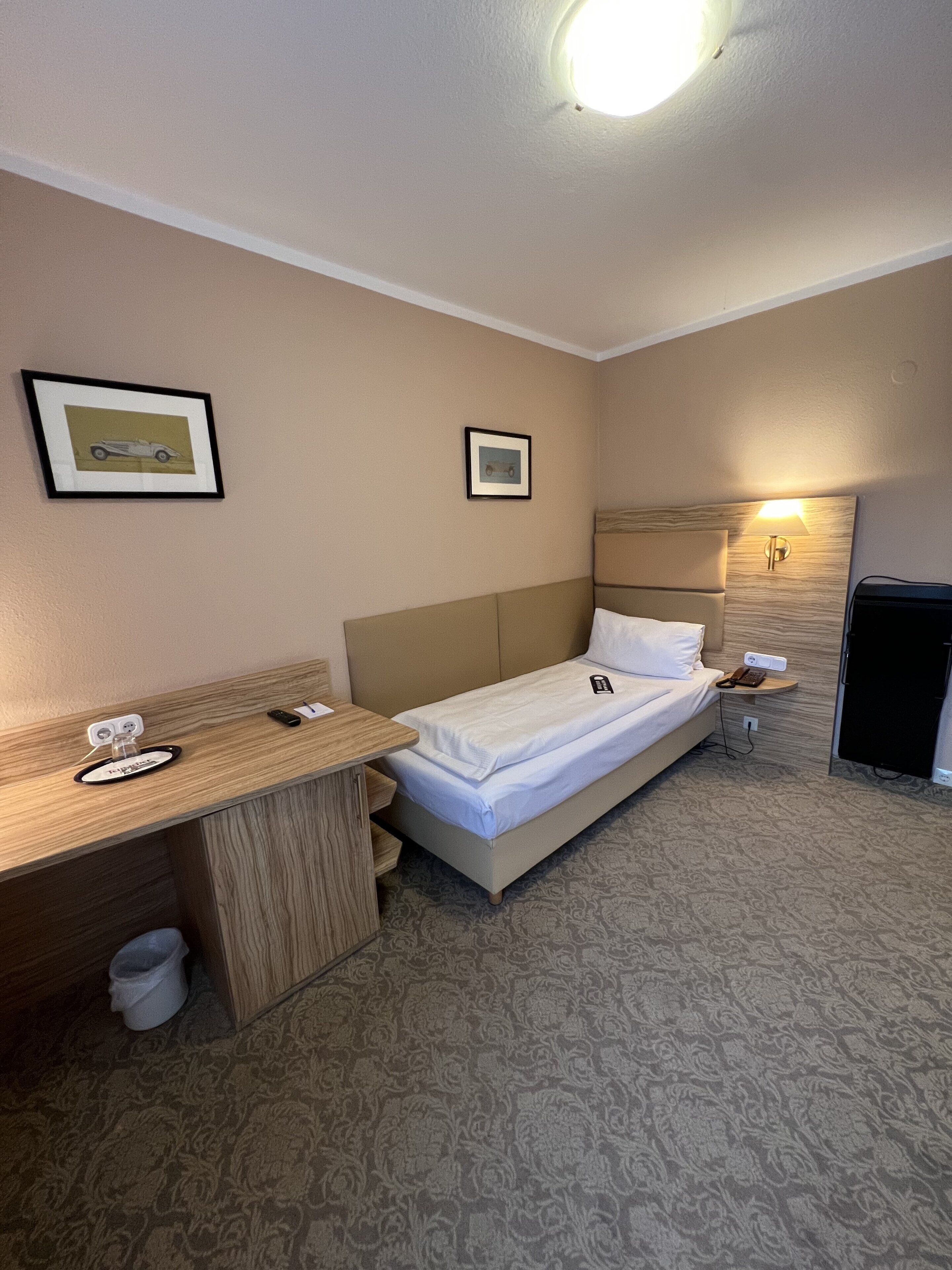 Una habitación de hotel con cama, escritorio, silla, lámpara y un refrigerador pequeño.
