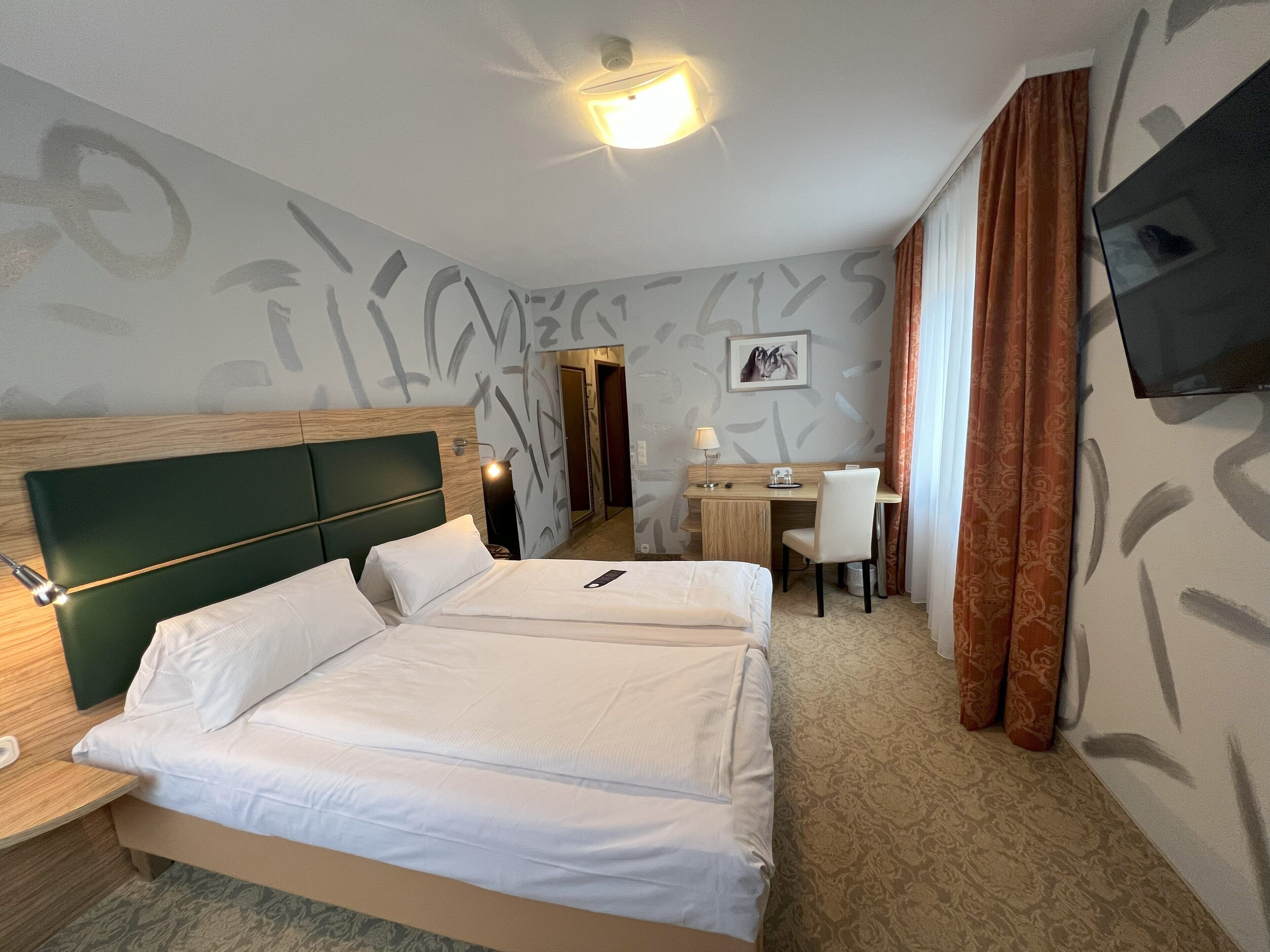 Een hotelkamer met een bed, bureau, stoel en een televisie aan de muur.