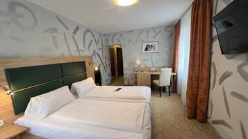 Een hotelkamer met een bed, bureau, stoel en een televisie aan de muur.
