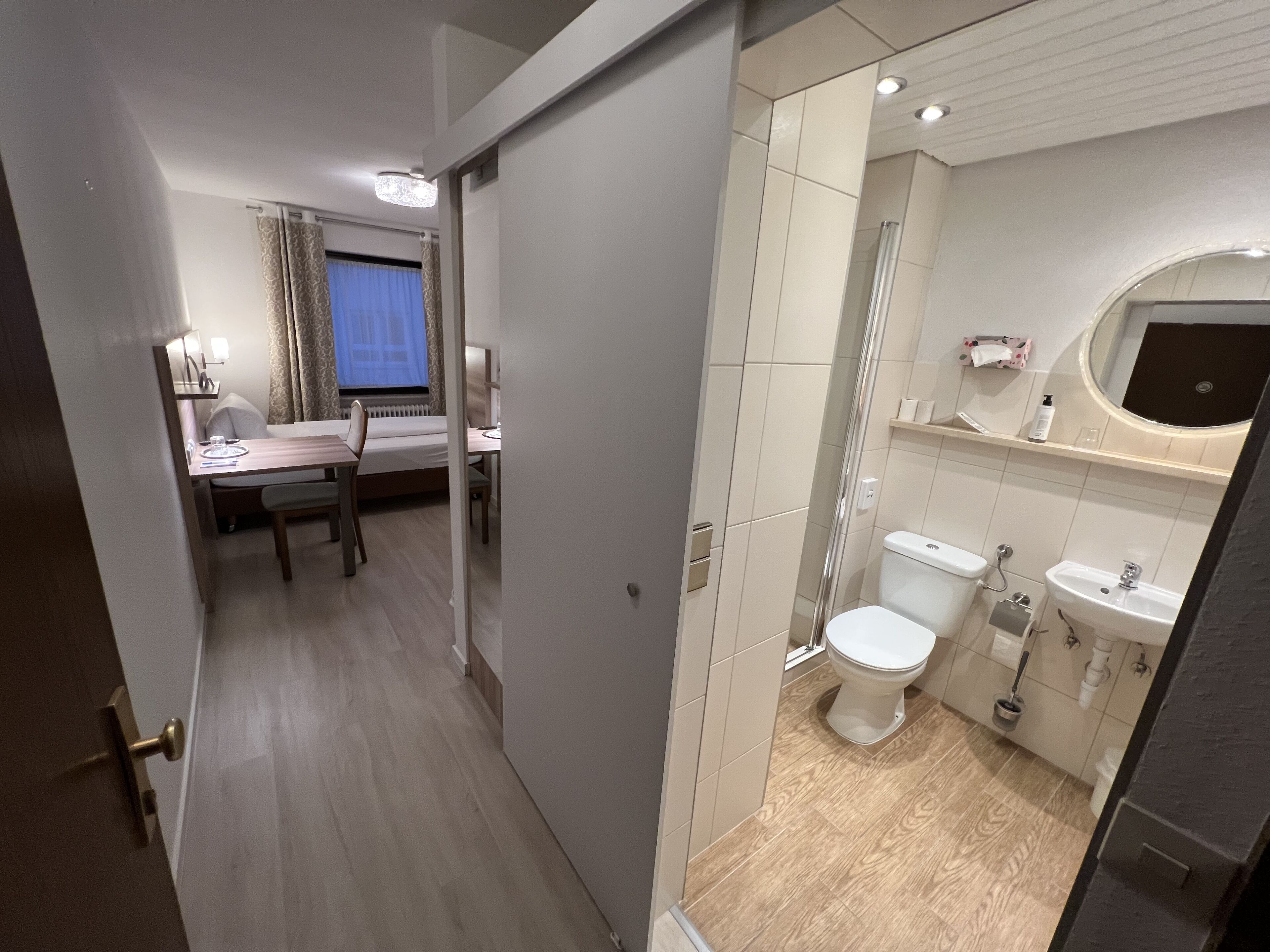 A hotel room with a dining area, a shower, and a bathroom with a toilet, sink, and mirror.