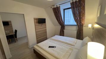 Una habitación de hotel con cama, escritorio, televisor y ventana con cortinas.