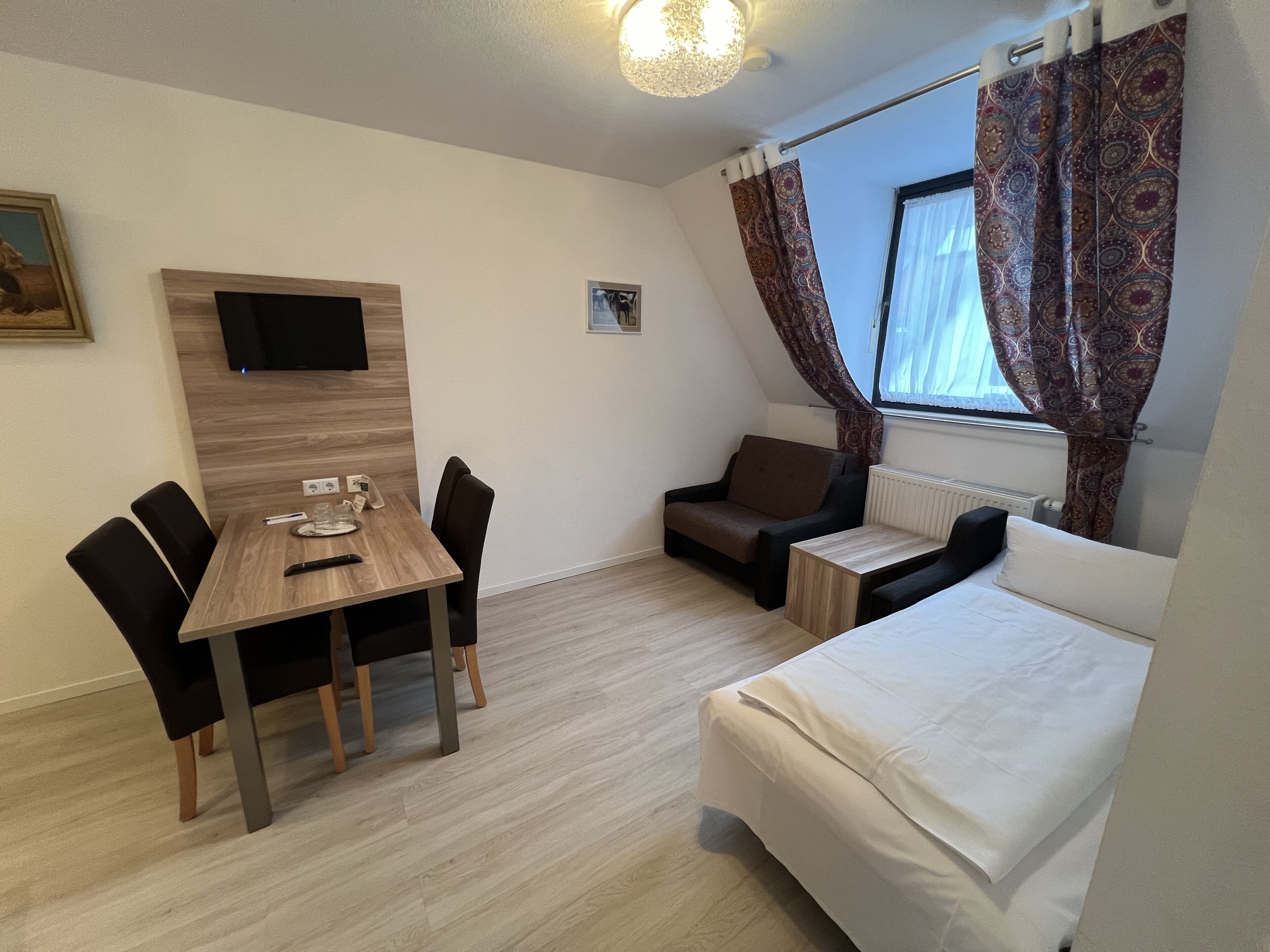 A compact room with a wooden dining table, two chairs, a sofa, and a single bed.