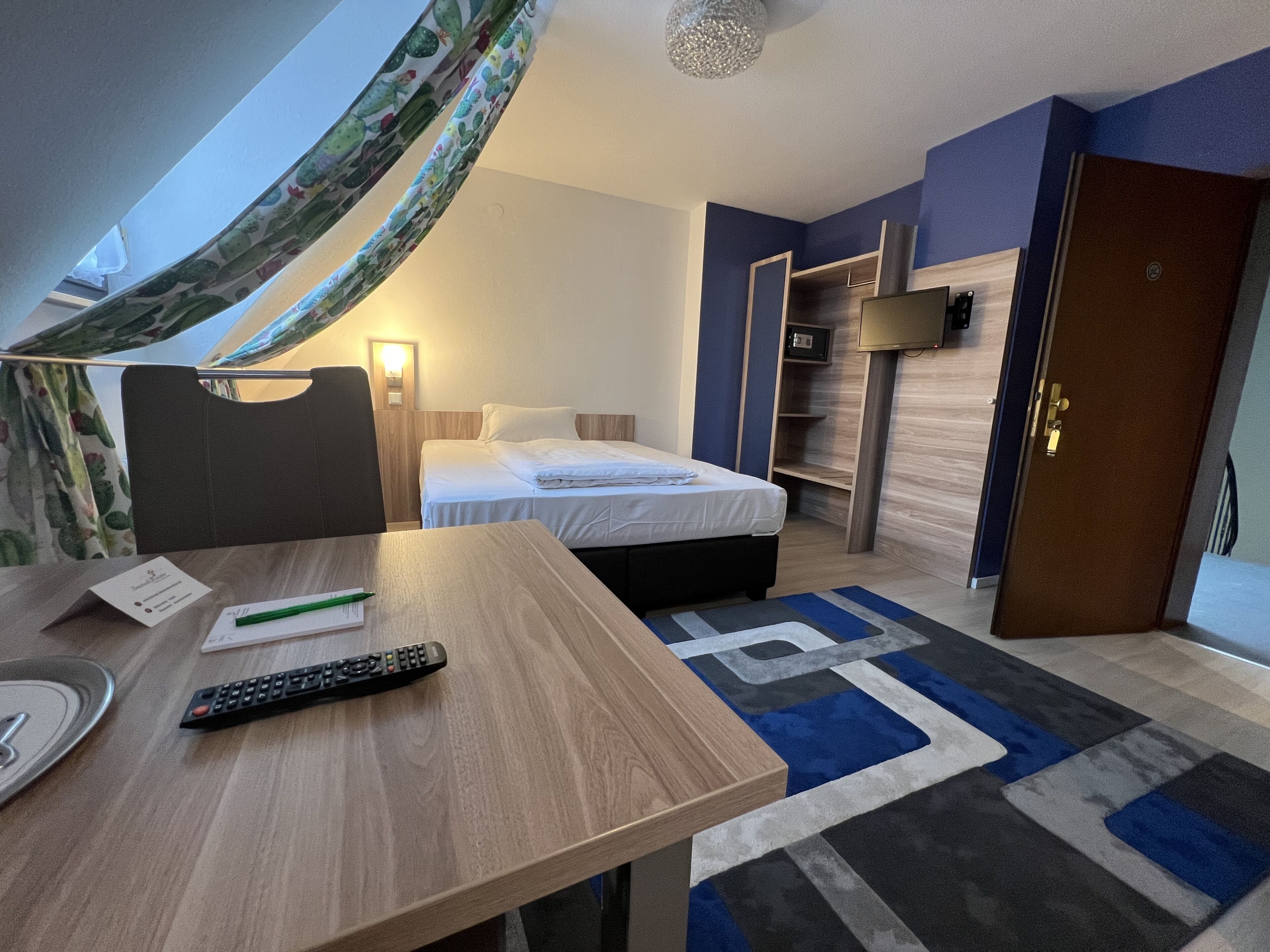 A hotel room with a bed, a desk with a remote control, a lamp, and a TV.