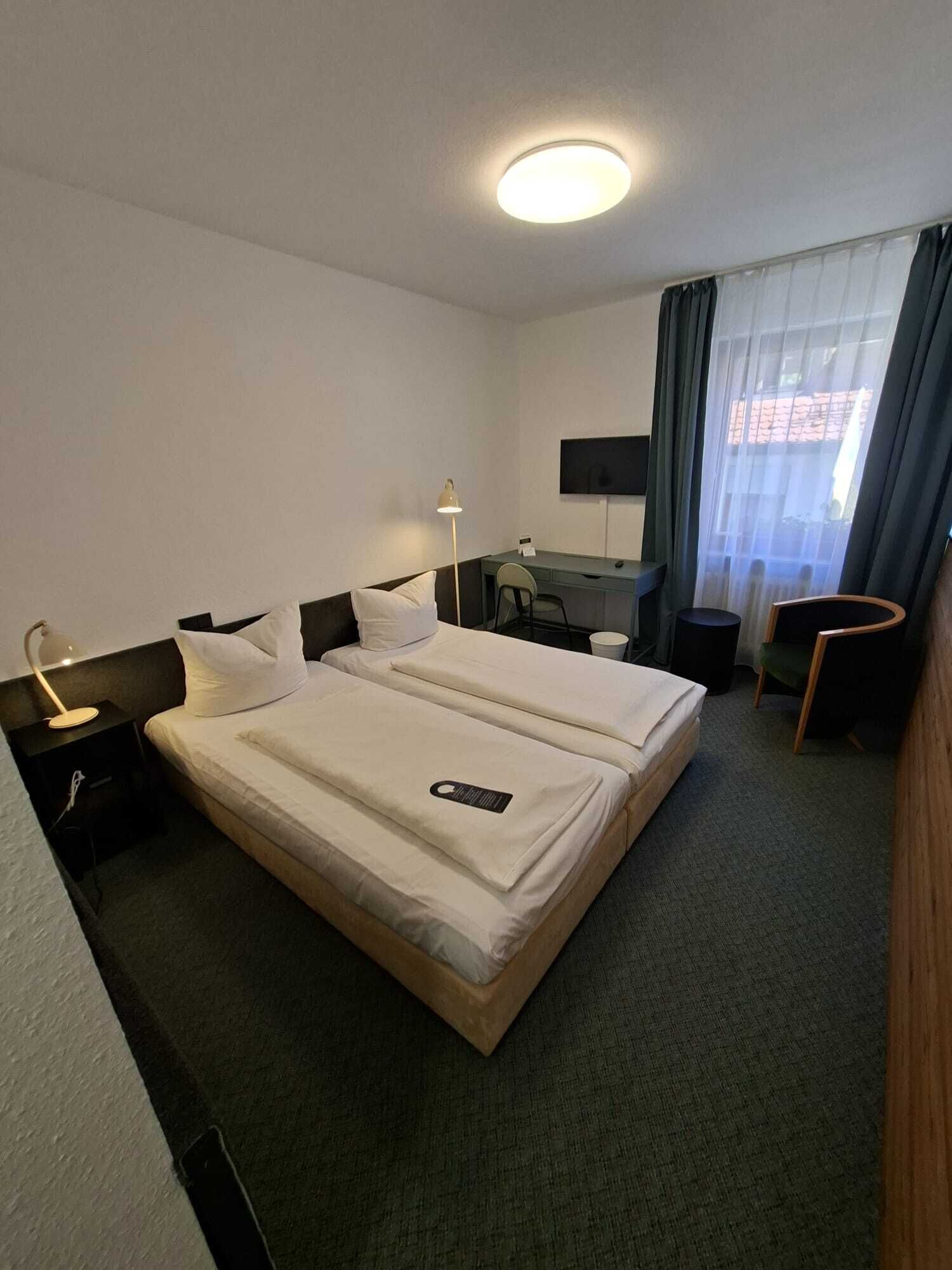 A hotel room with two beds, a desk, a chair, a TV, and a window with curtains.
