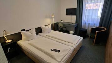 A hotel room with two beds, a desk, a chair, a TV, and a window with curtains.