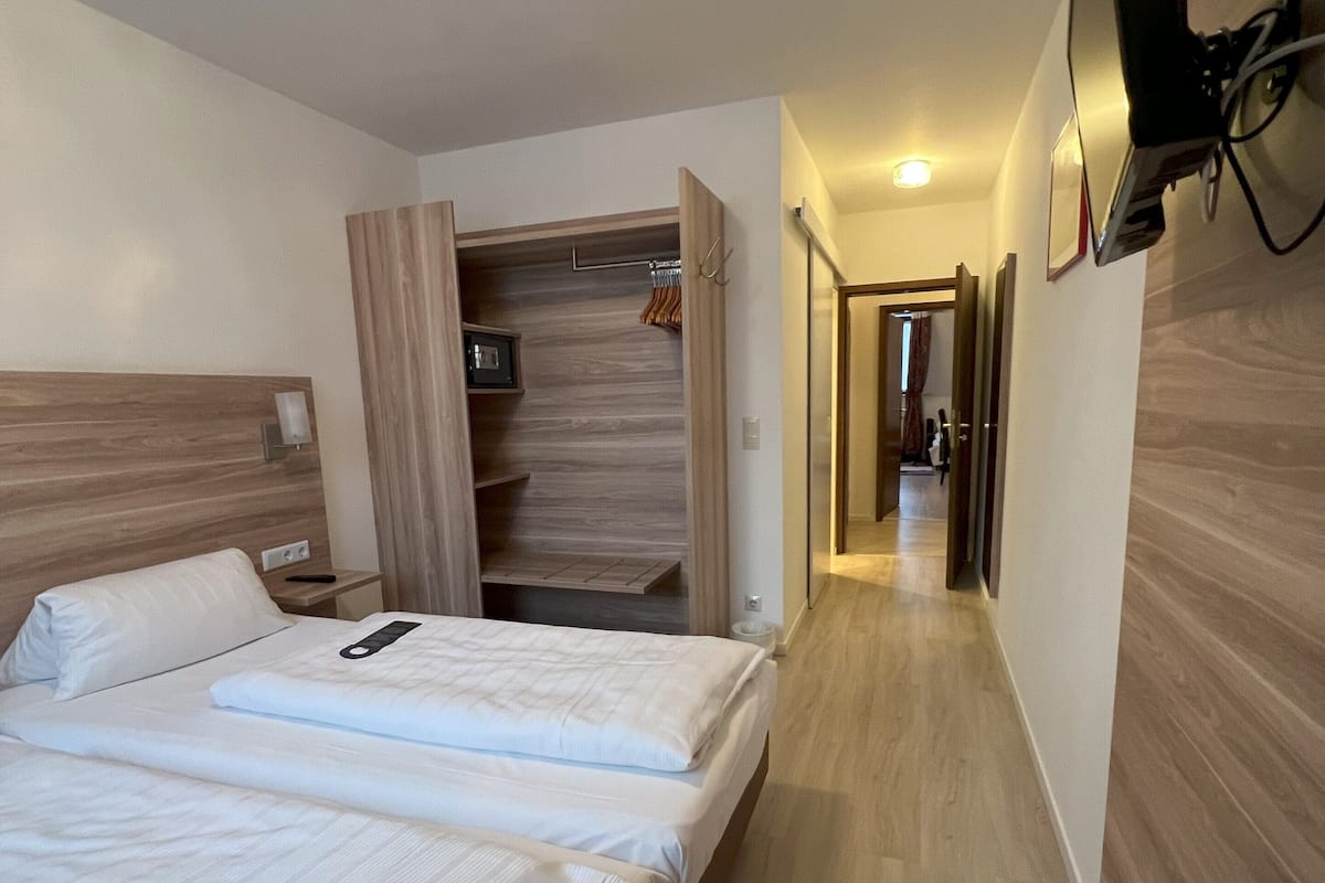 A hotel room with two beds, a walk-in closet, a TV mounted on the wall, and a hallway leading to another room.