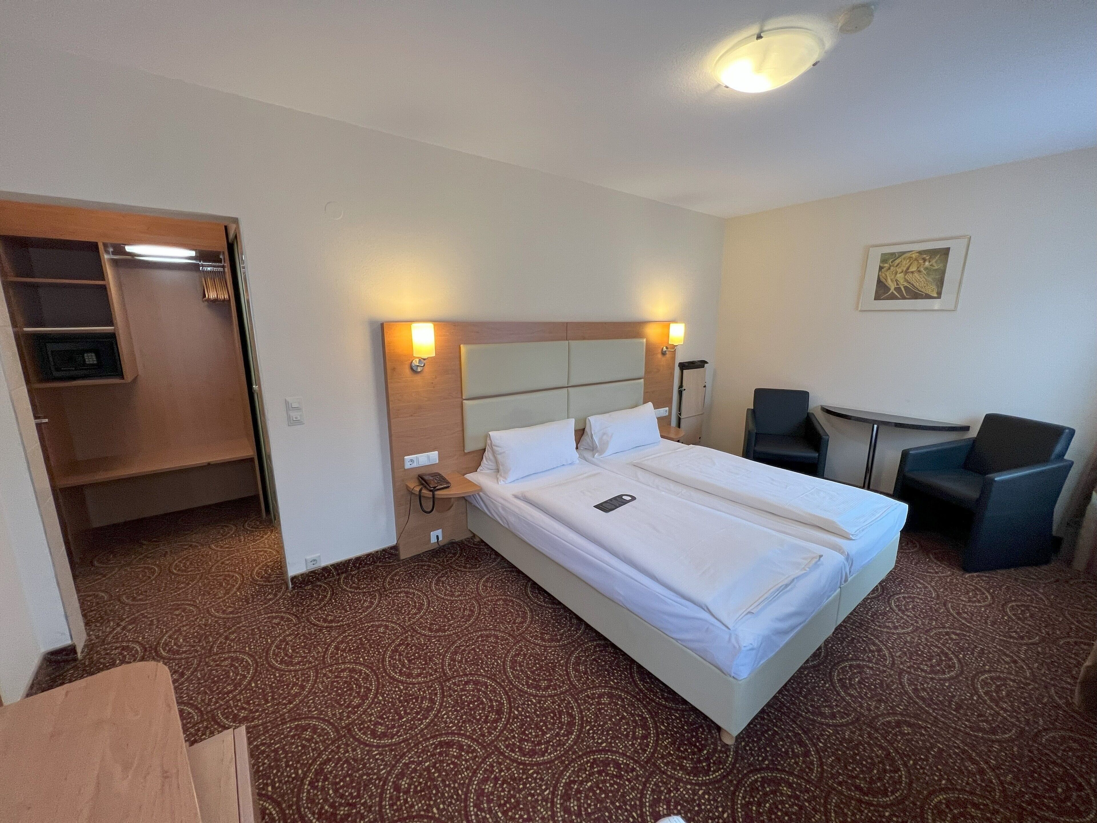 A hotel room with a large bed, bedside tables, a desk, two chairs, and a small seating area.