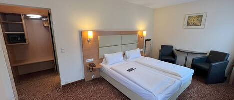A hotel room with a large bed, bedside tables, a desk, two chairs, and a small seating area.