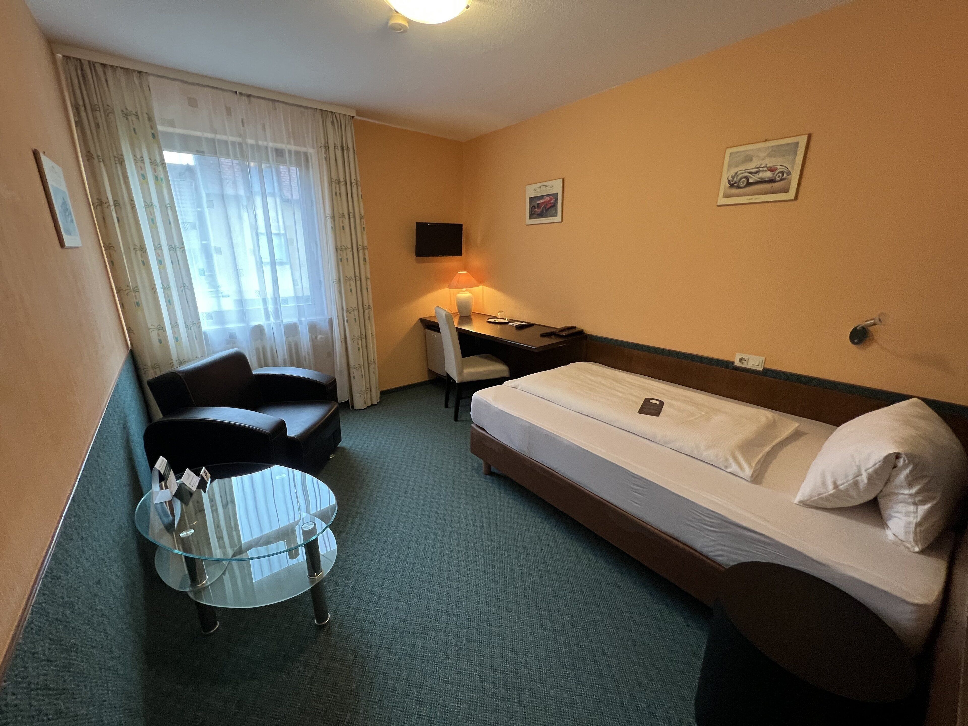 A hotel room with a bed, a desk, a chair, a glass table, and a window with curtains.