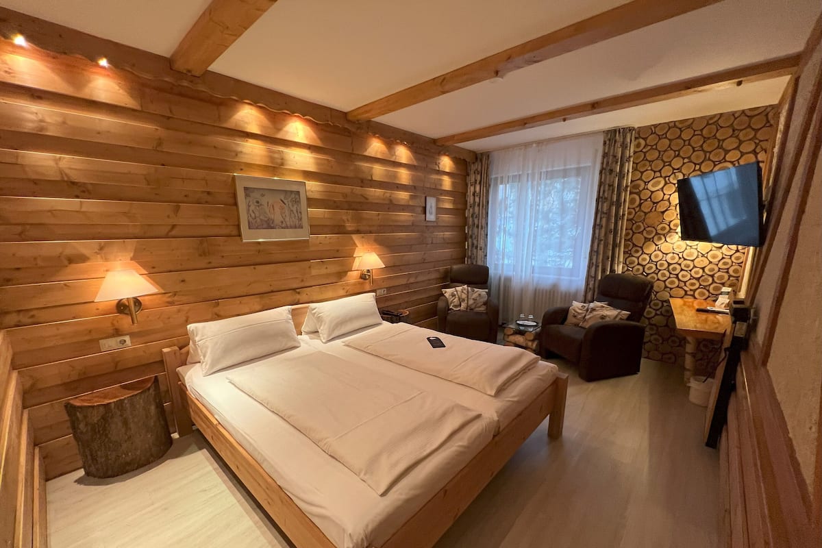 A wooden-paneled bedroom with a large bed, two chairs, a small table, and a TV.