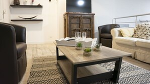 Uma sala de estar moderna com uma mesa de centro de madeira, duas cadeiras brancas, um sofá e uma TV sobre um móvel de madeira.