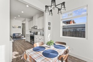 A modern kitchen with white cabinets, a dining area with a plaid tablecloth, and a view of a wooden deck. - Cozy Oakland Home  (Oakland)