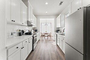 A modern kitchen with white cabinetry, a central island, and a dining area with a table and chairs. - Cozy Oakland Home  (Oakland)