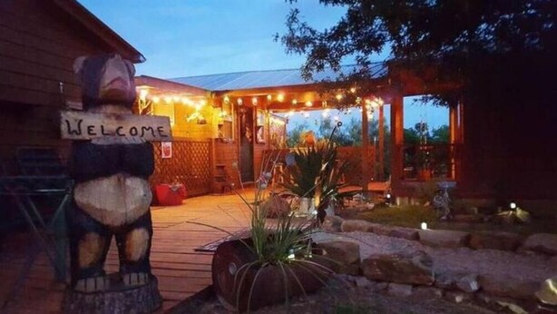 Una cabana de fusta amb un rètol que diu 'Welcome', un porxo cobert amb llums de garlandes i una zona d'estar a l'aire lliure rústica.