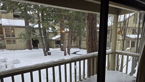 A wooden deck with snow on the railing and ground, overlooking a residential area with houses and trees.