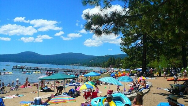 A beach with people, umbrellas, and a pier in the background.