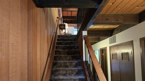 A wooden staircase with a handrail, leading to a landing with a door and a window.