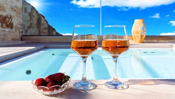 Two glasses of wine and a bowl of strawberries by a pool with a clear blue sky. - Akalli Villa Private Pool & Hot Tub (Paraskevi)