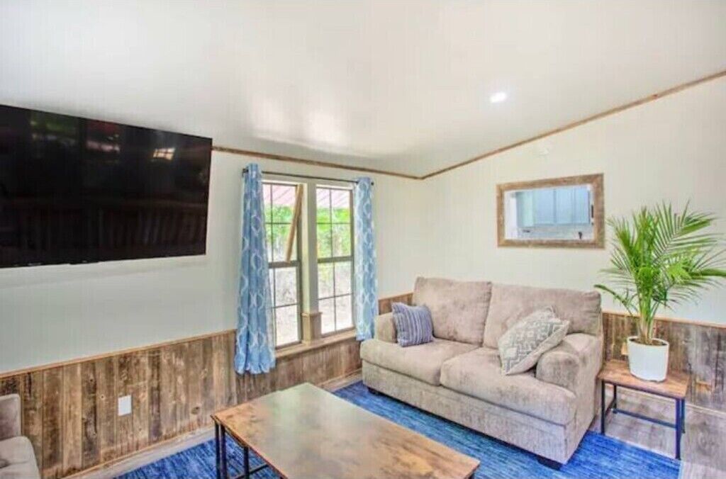 A living room with a sofa, a coffee table, a TV, and a window with curtains.