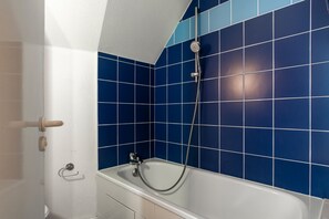 Um banheiro com banheira e chuveiro, paredes azulejadas em azul e teto branco.