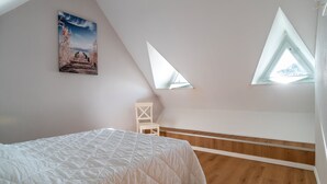 Une chambre avec un plancher en bois, un lit blanc et deux fenêtres de toit.