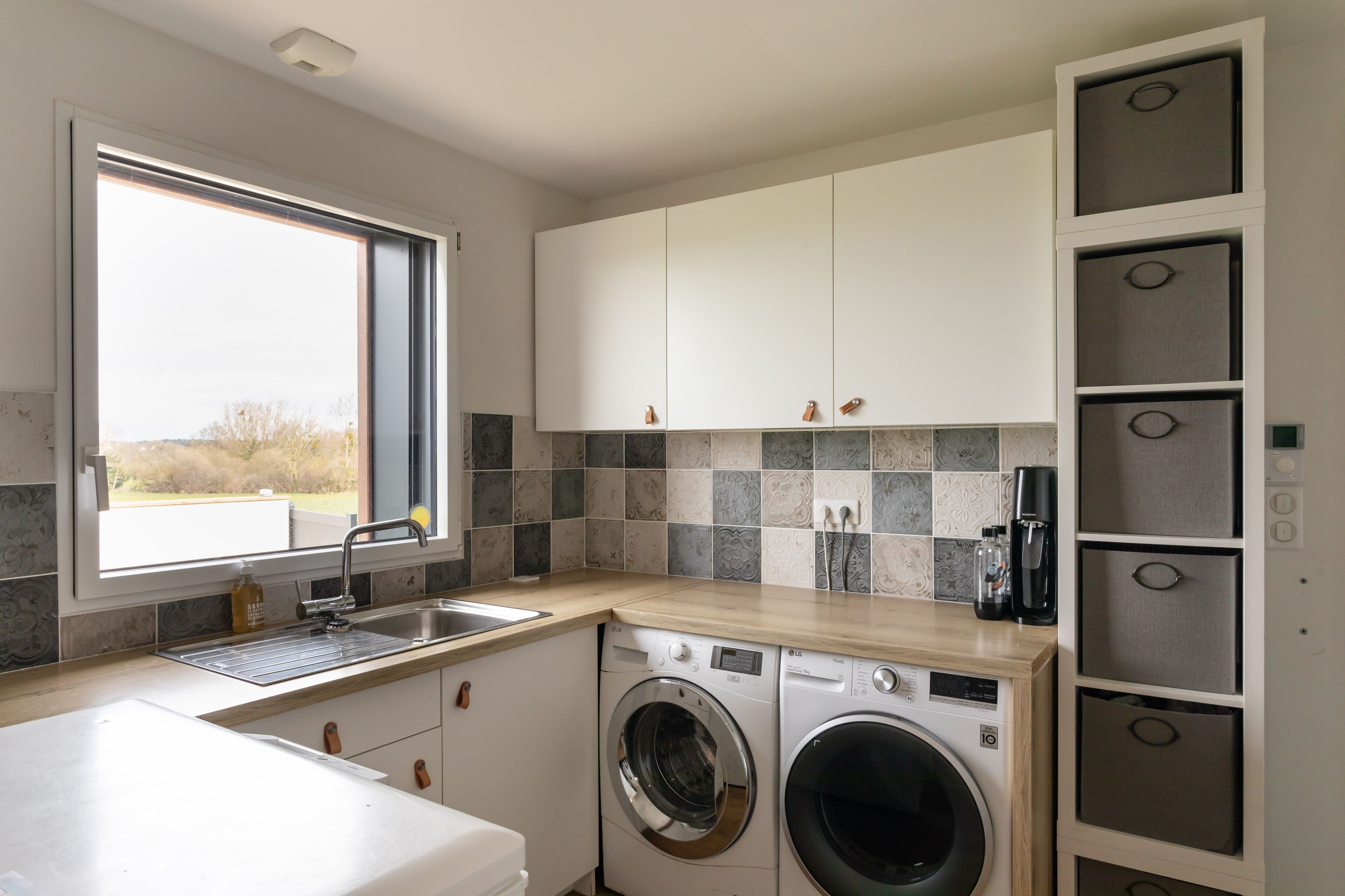 Een moderne keuken met een ingebouwde wasmachine en droger, een groot raam en een betegelde spatwand.