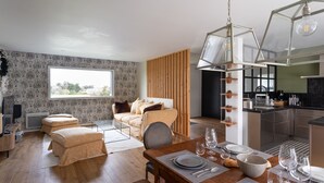 A modern hotel room with a large window, a wooden partition, a dining area with a table set for four, and a kitchenette. - La perle de mer - Charmante maison avec jacuzzi (Erquy)