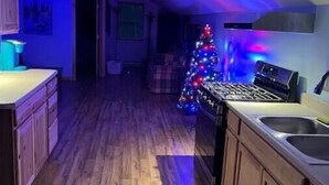Une cuisine étroite avec des meubles en bois, un four encastré et un four à micro-ondes. On aperçoit un sapin de Noël illuminé de guirlandes colorées à l’arrière-plan.