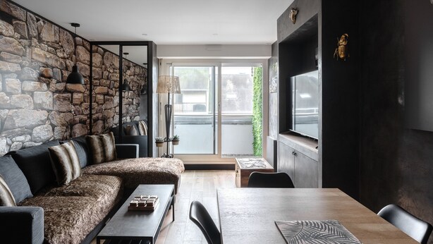 A modern living room with a stone wall, a sofa, a dining table, and a TV.