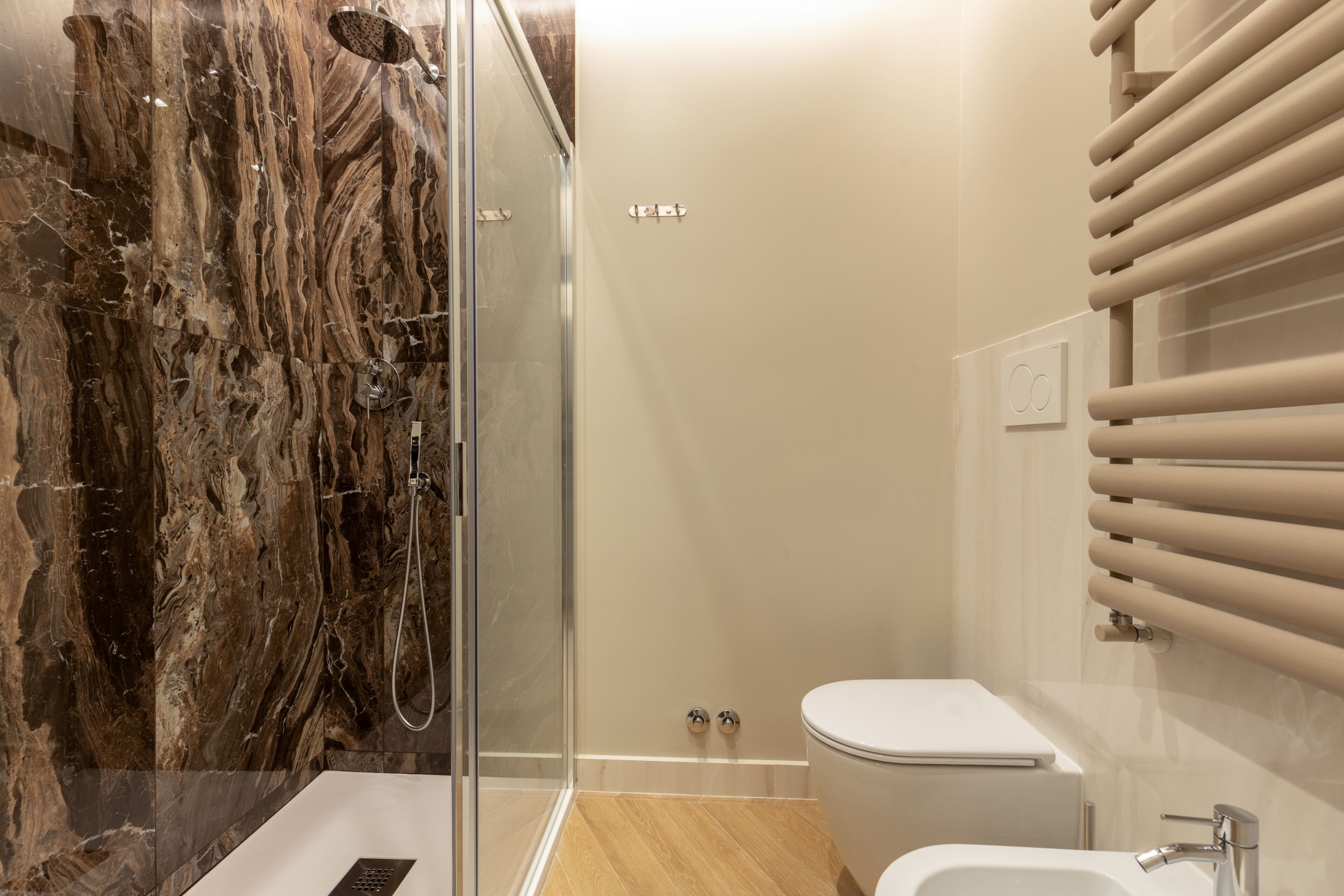 Un baño moderno con pared de ducha de mármol, cabina de ducha con puerta de cristal, inodoro y lavamanos con grifo.