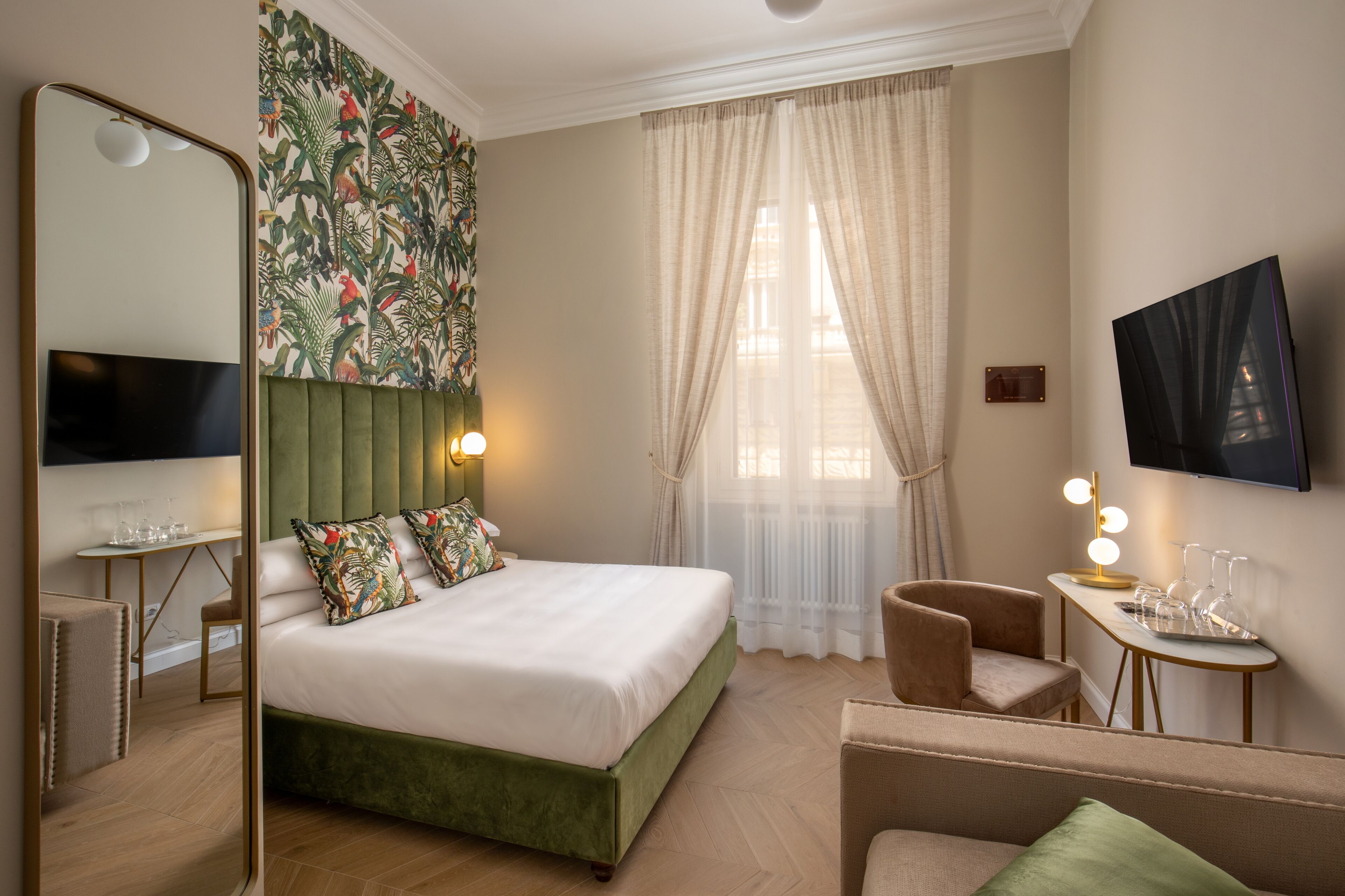 A hotel room with a bed, a seating area, a television, and a table with glasses.