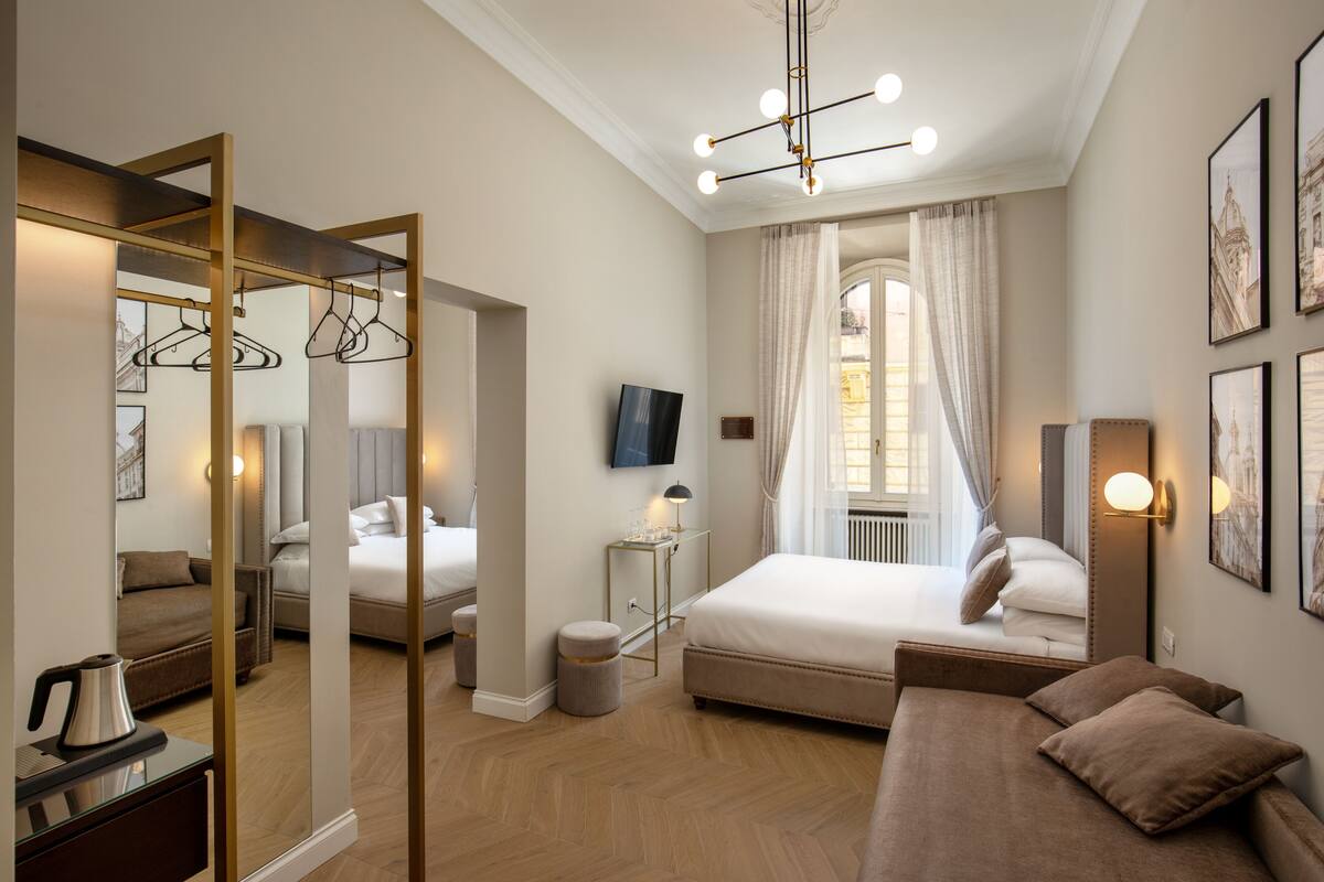 Une chambre d’hôtel avec un grand miroir, un lit, un canapé, une télévision et une fenêtre avec des rideaux.