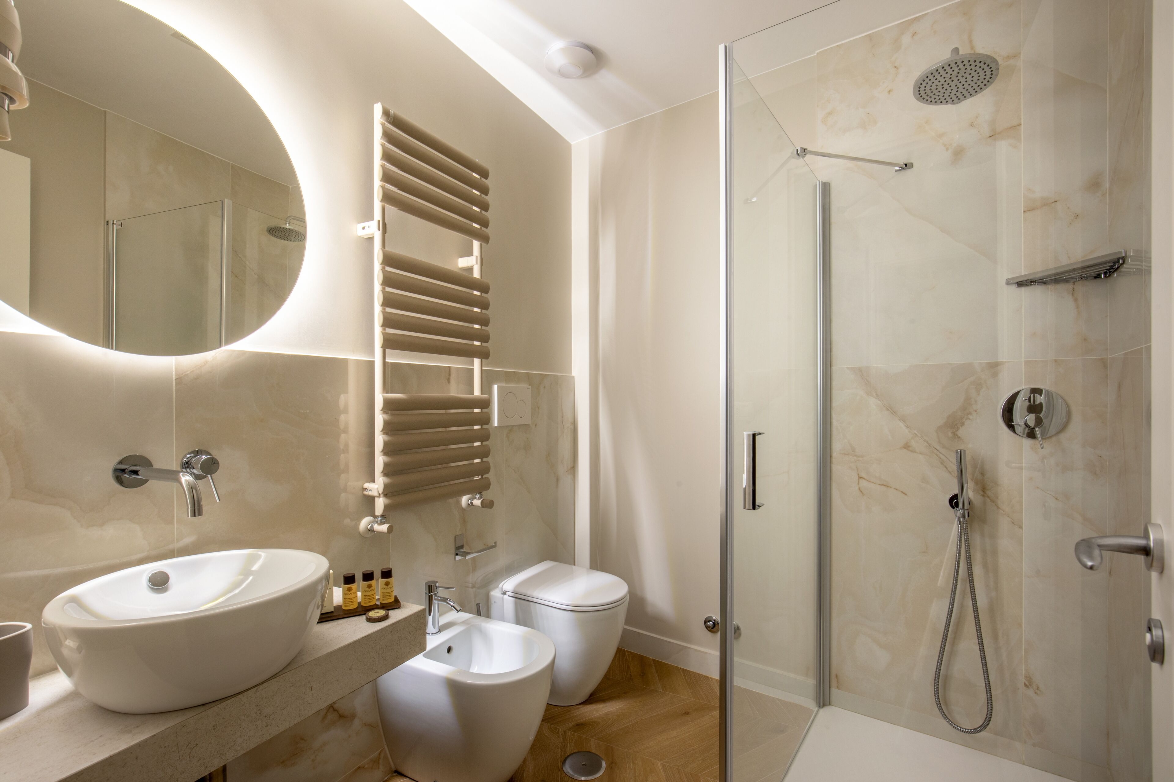 A modern bathroom with a large oval sink, a bidet, a toilet, and a glass-enclosed shower area.