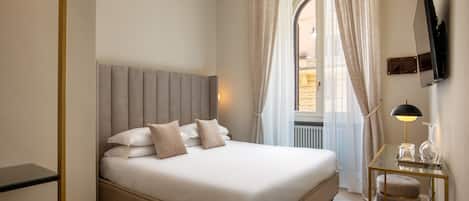 A neatly made bed with a headboard, a bedside table with a lamp, and a view of the outdoors through a window with curtains.