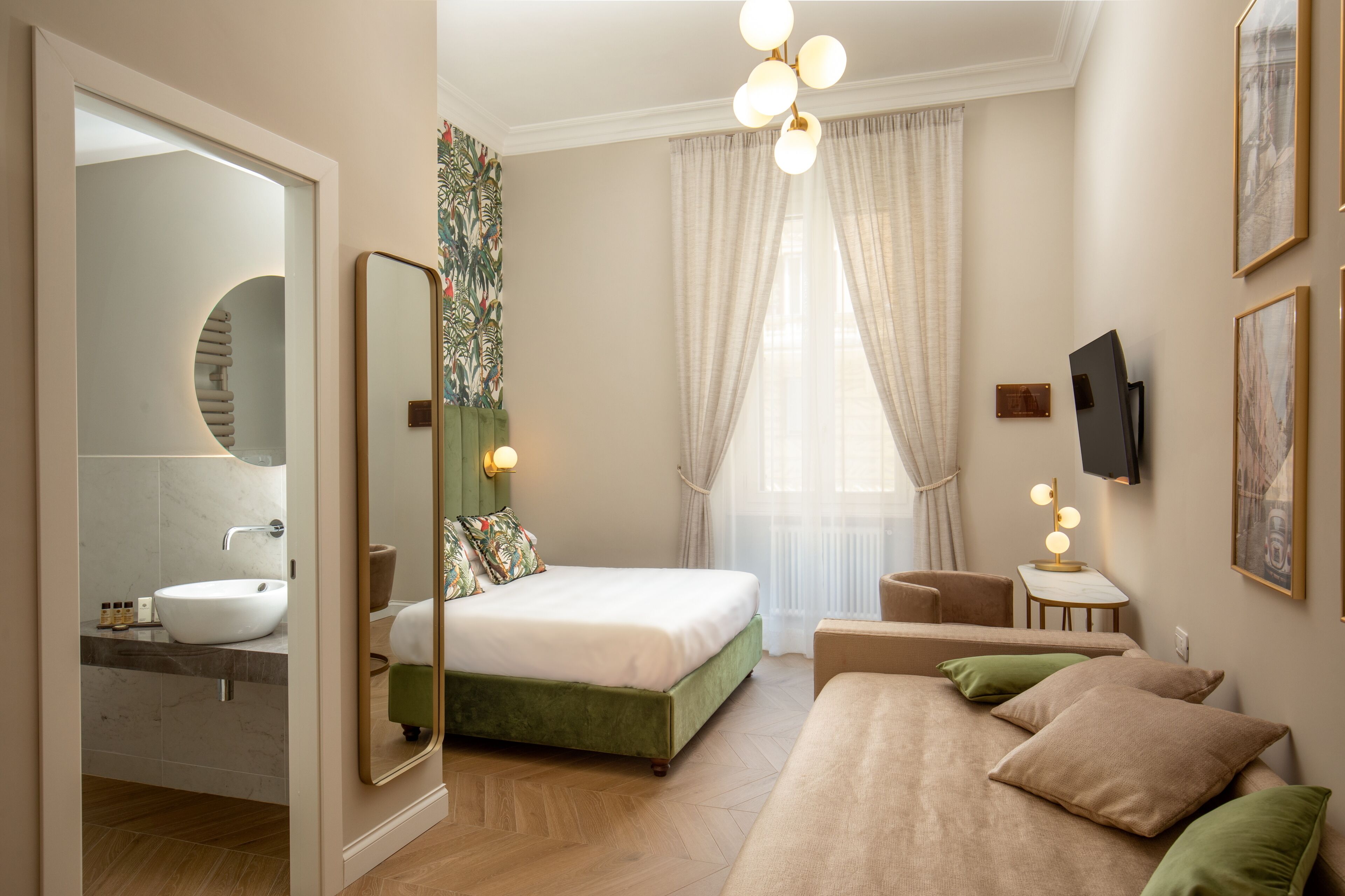 Ein modernes Schlafzimmer mit einem großen Bett, einem Schminktisch mit Waschbecken, einem Fernseher und einem grünen Sofa.
