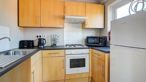 Uma cozinha compacta com armários de madeira, fogão a gás, micro-ondas e geladeira.