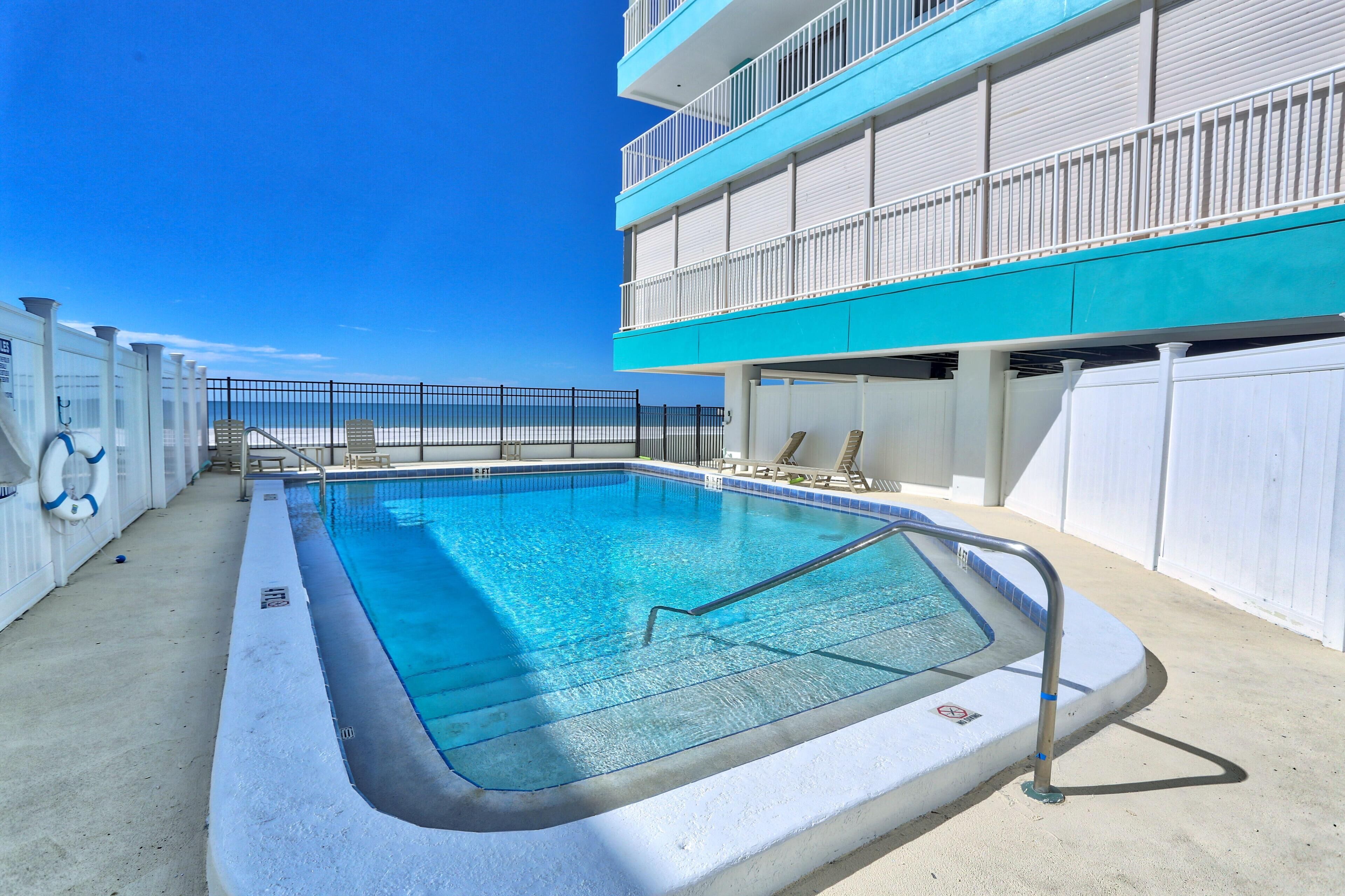 A swimming pool with a metal ladder, surrounded by a white building with balconies.