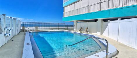A swimming pool with a metal ladder, surrounded by a white building with balconies.