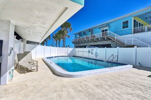A swimming pool with a white deck, a covered area with lounge chairs, and a staircase leading to a blue building with a balcony. - Arena De Madeira 502- Premier (Madeira Beach)