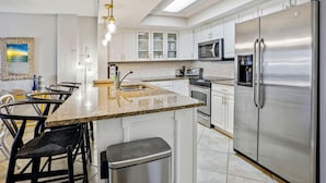 A modern kitchen with white cabinets, a stainless steel refrigerator, a built-in oven, and a granite countertop. - Arena De Madeira 502- Premier (Madeira Beach)