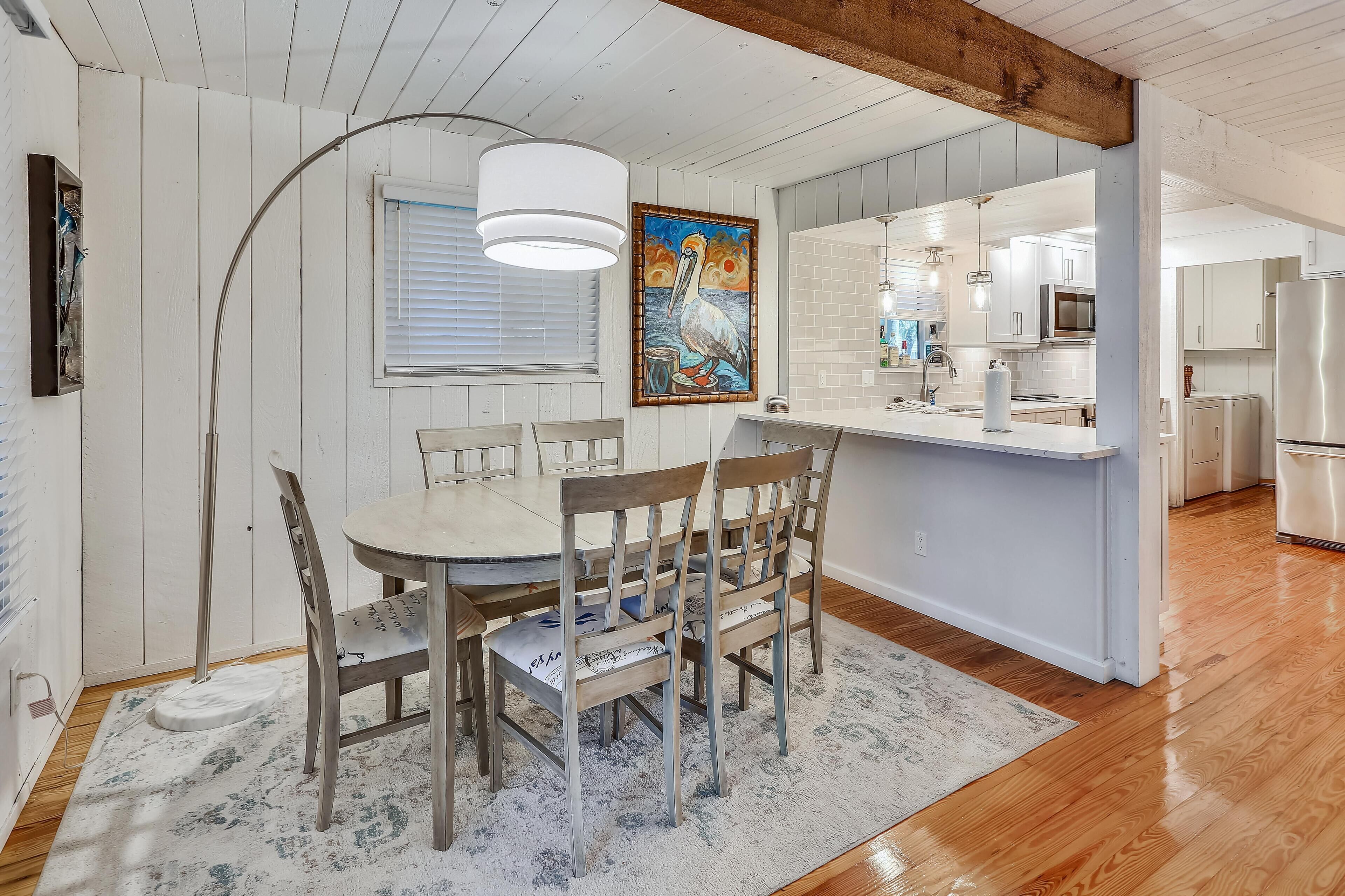 A modern kitchen with white cabinets, a stainless steel refrigerator, and a dining area with a wooden table and chairs.